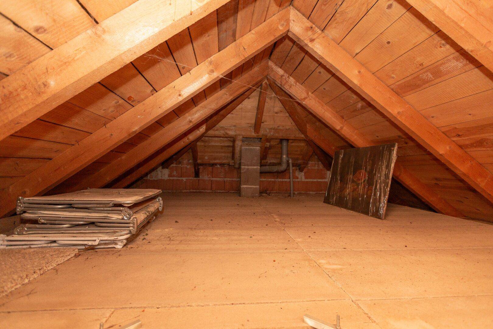 Unausgebauter Dachboden mit sichtbaren Holzbalken und Stauraum.