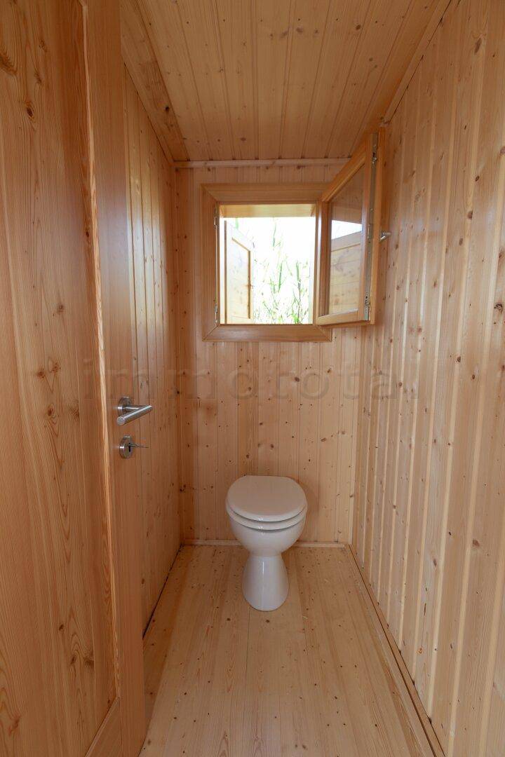Kleines WC mit Holzvertäfelung, einem Fenster und einfacher Toilette.