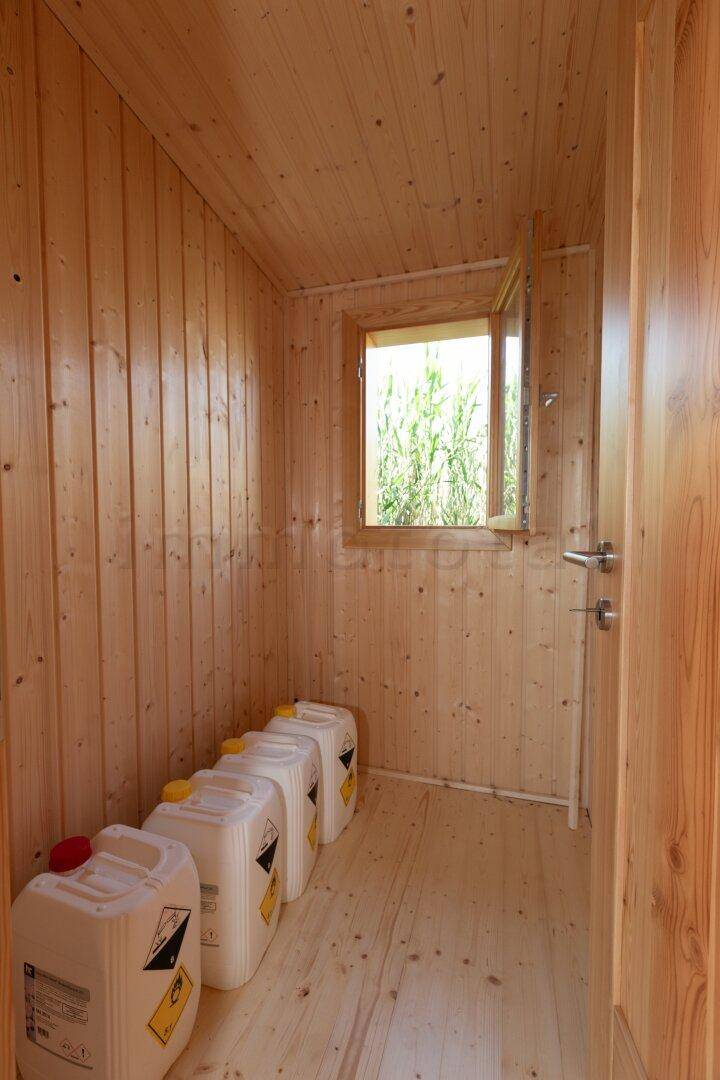 Einfacher Abstellraum mit Holzvertäfelung, einem Fenster und gelagerten Behältern.