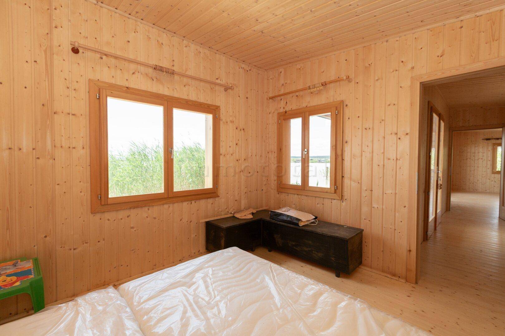 Helles Schlafzimmer mit zwei Fenstern, Holzvertäfelung und Blick auf die umliegende Natur.