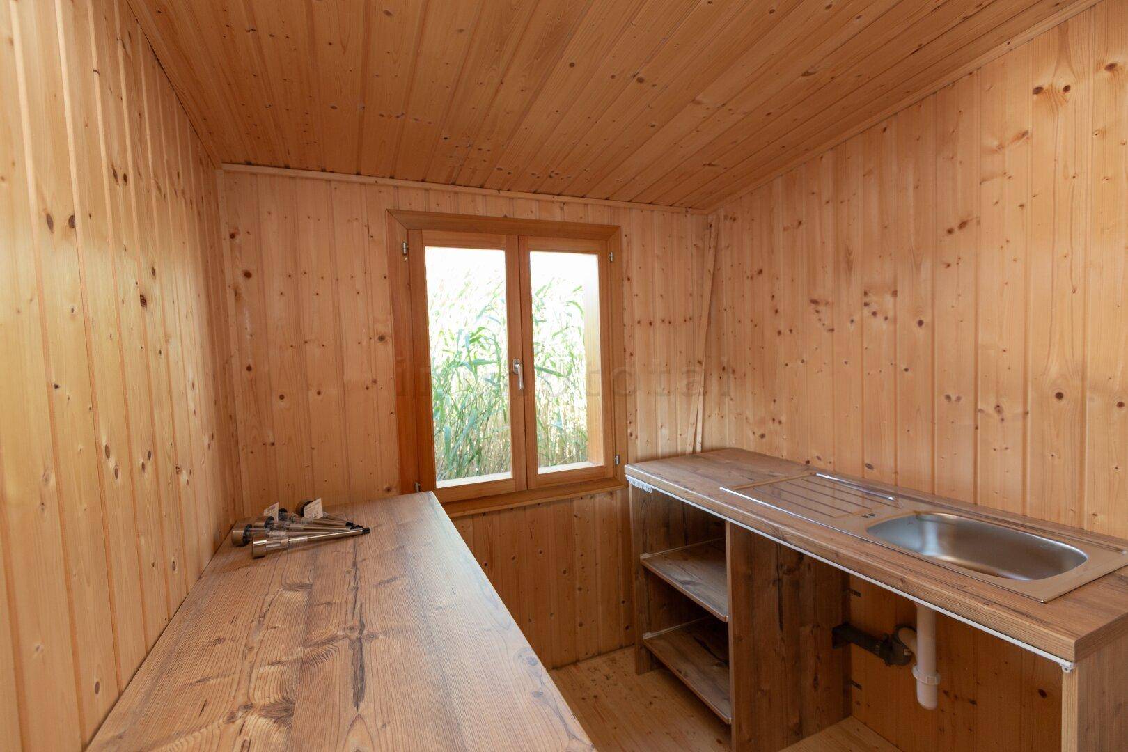 Einfache Küche mit Holz-Arbeitsplatten, Spülbecken und einem Fenster mit Blick ins Grüne.