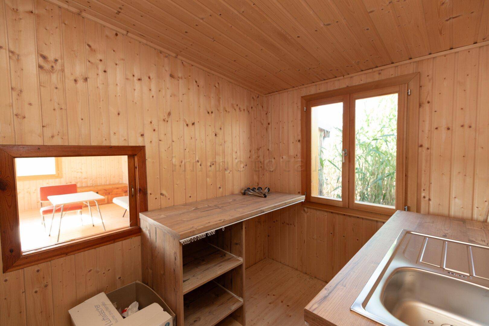 Kleine Küche mit Holz-Arbeitsplatten, Spülbecken und Durchreiche zum angrenzenden Wohnbereich.