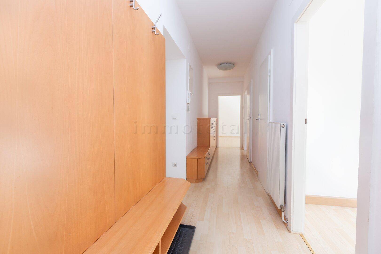 Langer, heller Flur mit Laminatboden und Garderobenmöbeln aus hellem Holz.