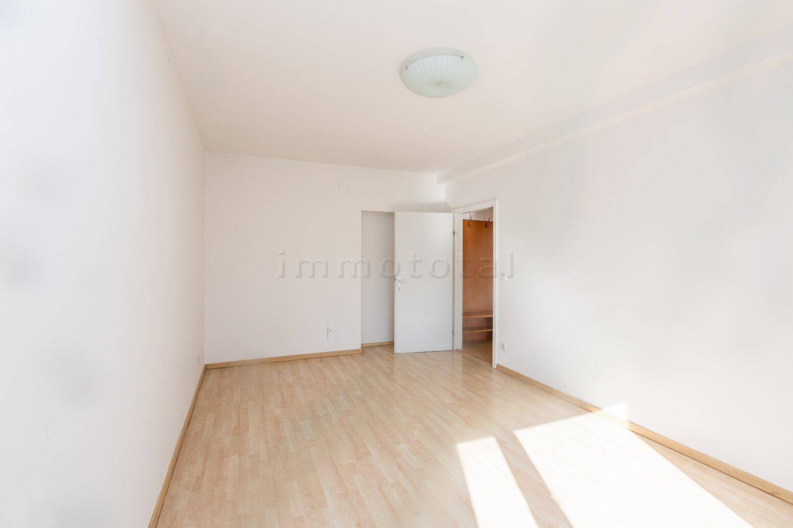 Helles, leeres Zimmer mit Laminatboden und weiß gestrichenen Wänden, bereit zur Einrichtung.