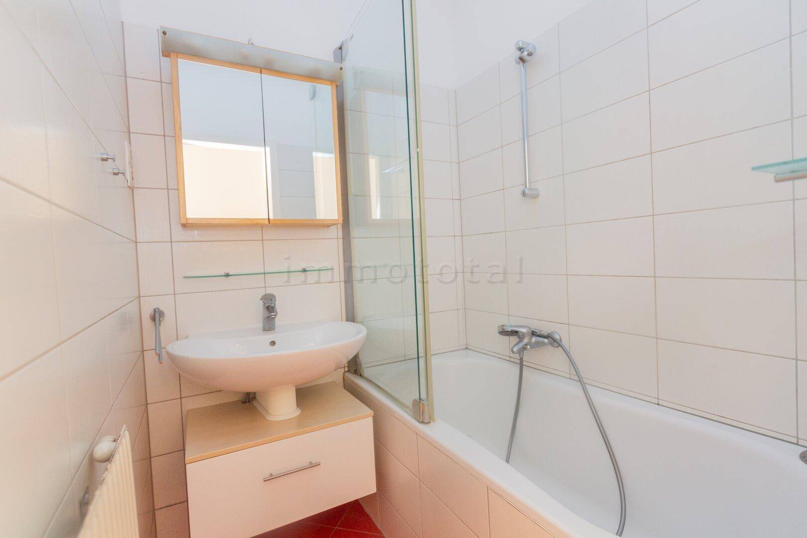 Badezimmer mit Badewanne, Duschabtrennung und Waschbecken, gefliest in Weiß und Rot.