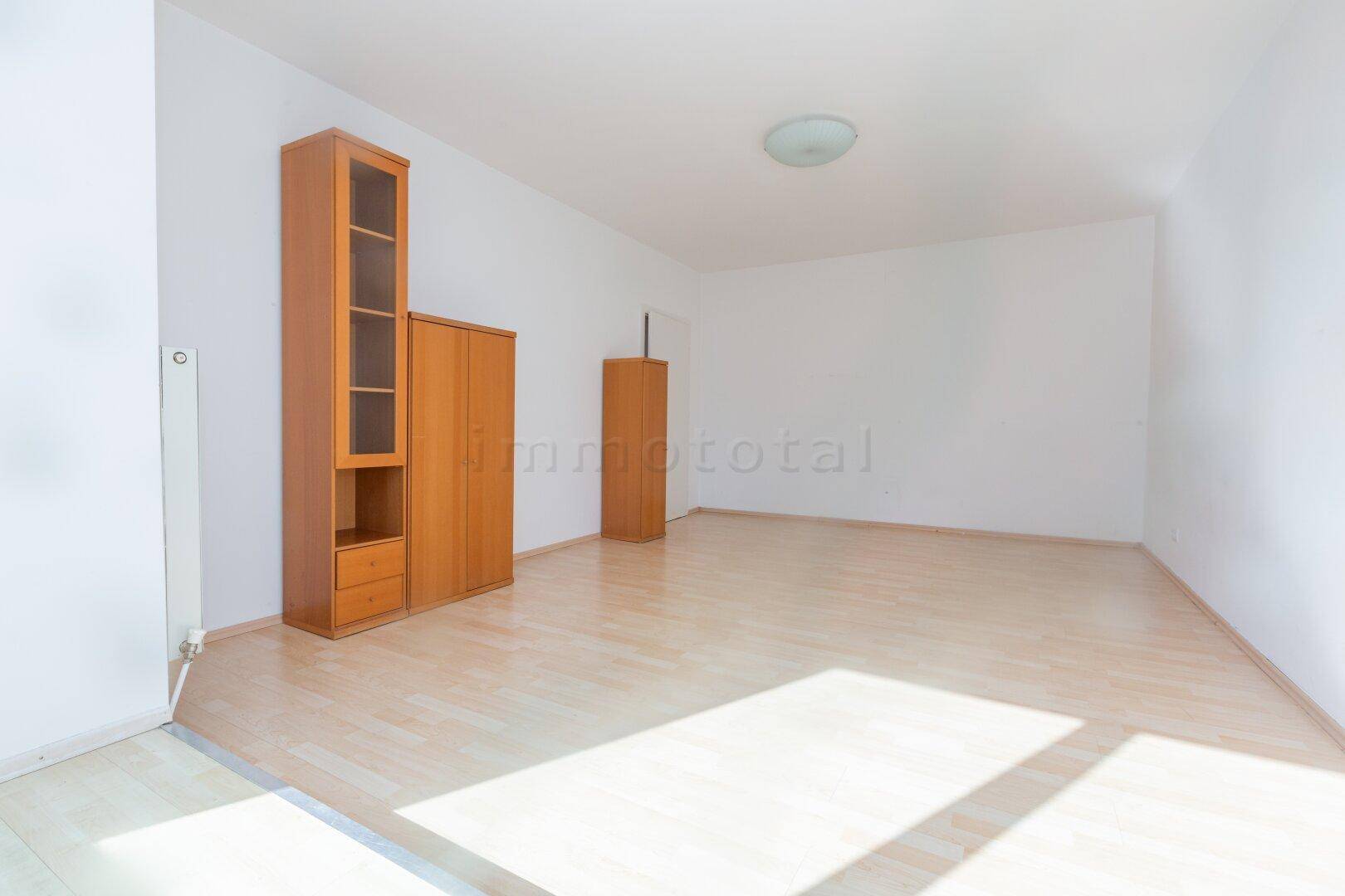 Geräumiges, helles Zimmer mit Laminatboden und Holzschränken, ideal als Wohnbereich.