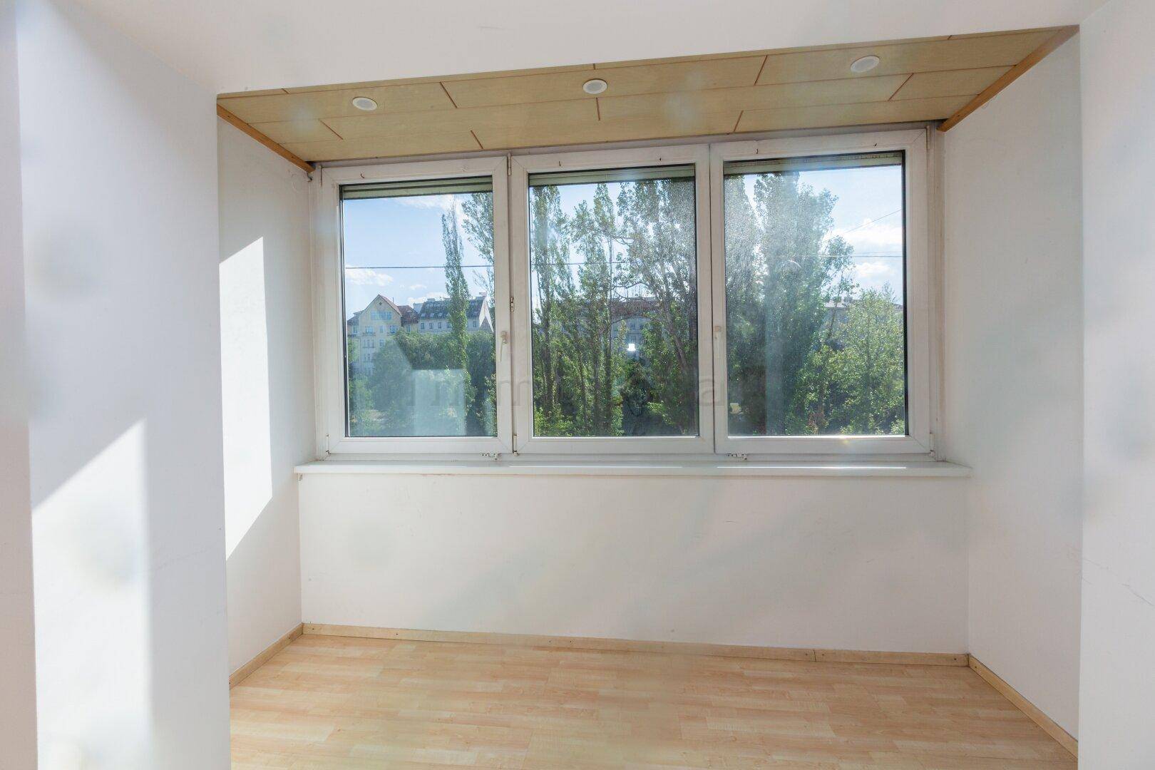 Heller, verglaster Raum mit Holzdecke und großen Fenstern, die viel Licht hereinlassen.
