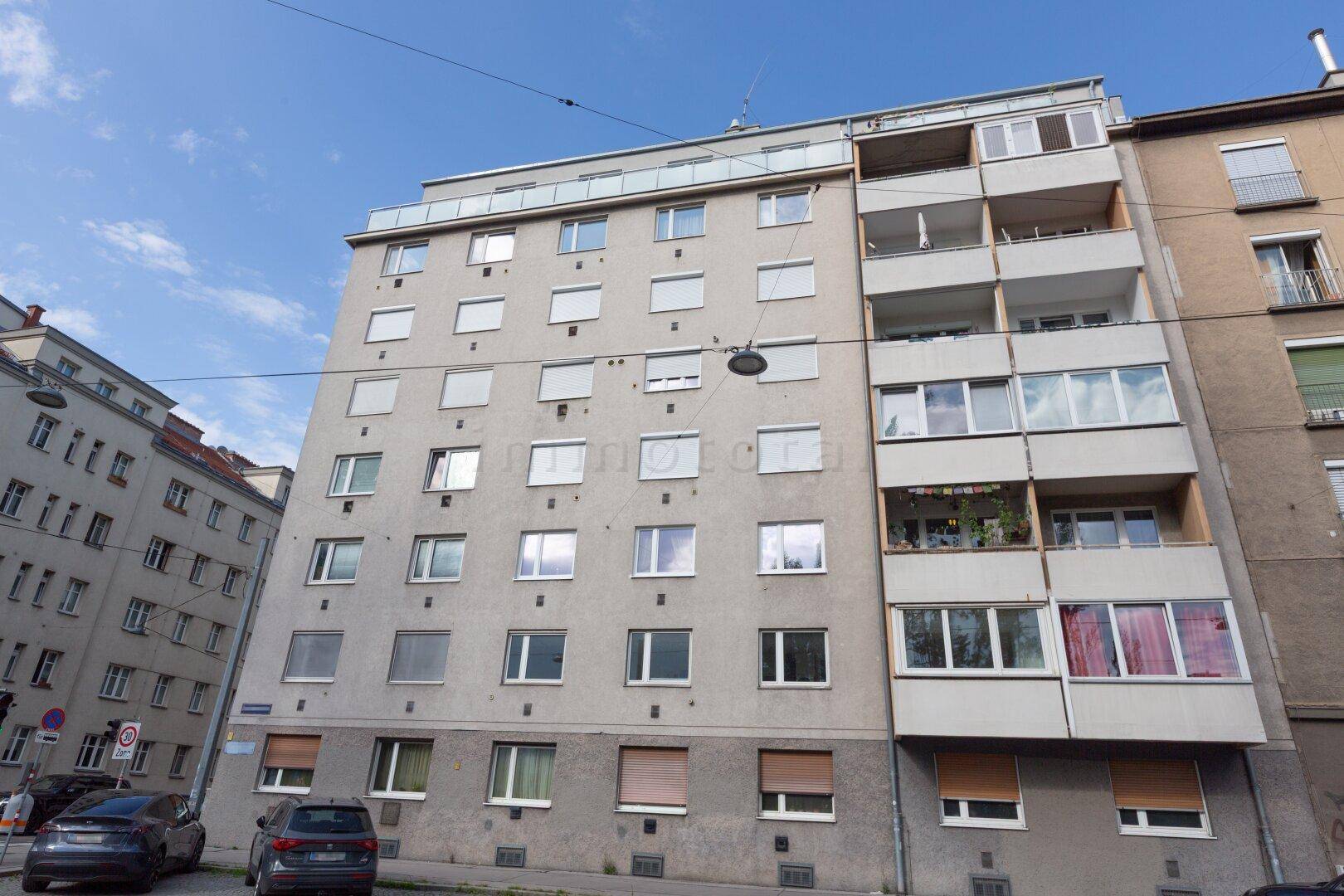 Mehrstöckiges Wohngebäude mit grauer Fassade, vielen Fenstern und Balkonen.