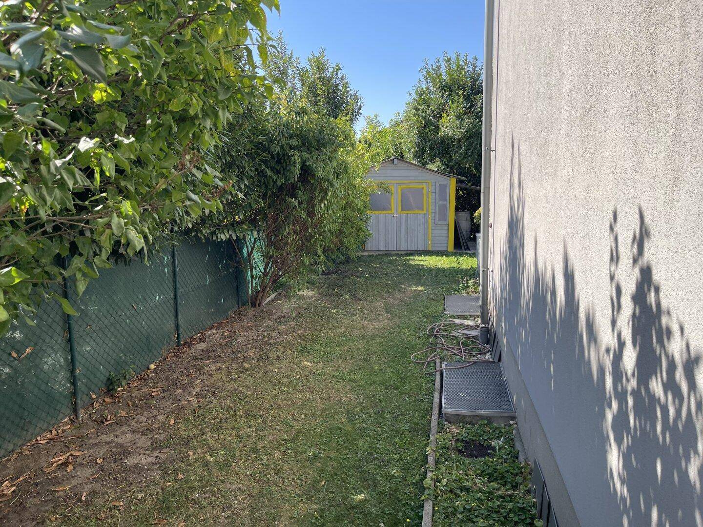Seitlicher Gartenbereich mit Rasenfläche, Zaun und Gartenhaus.