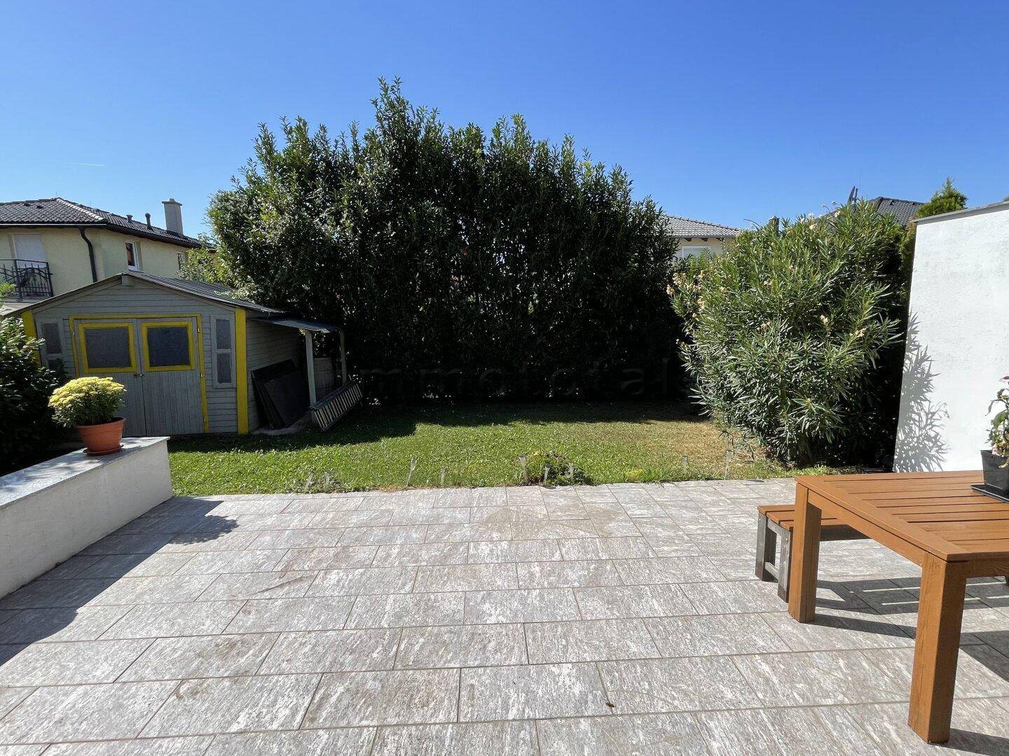 Großer, sonniger Garten mit gepflasterter Terrasse und Gartenhaus.