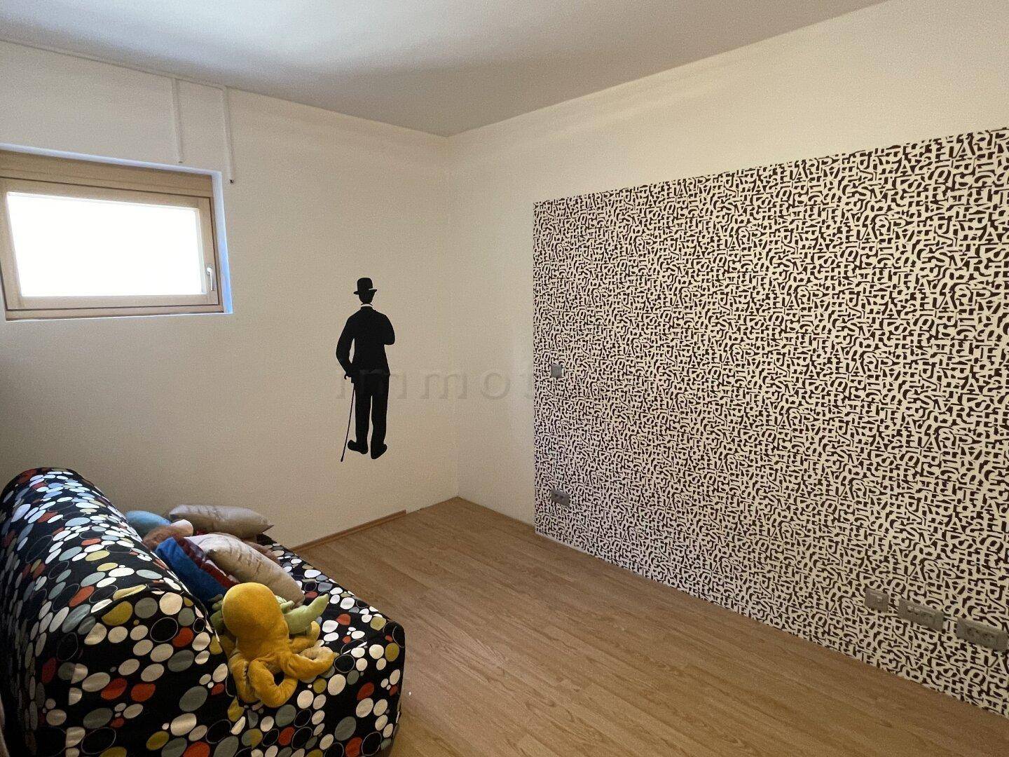 Zimmer mit auffälliger Mustertapete und Holzboden, vielseitig nutzbar.
