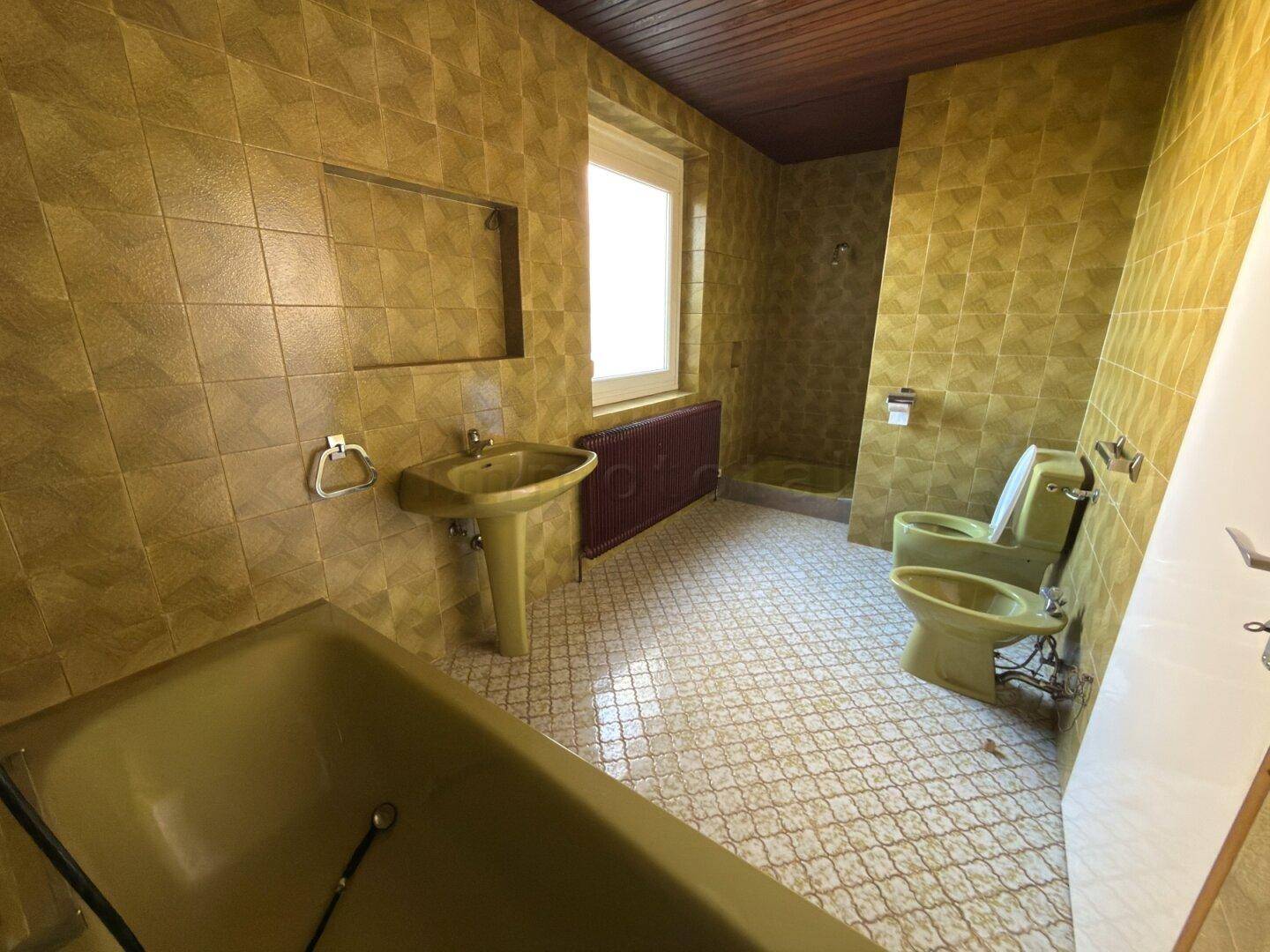 Badezimmer im Stil der 80er Jahre mit grünen Fliesen, Badewanne und Bidet.