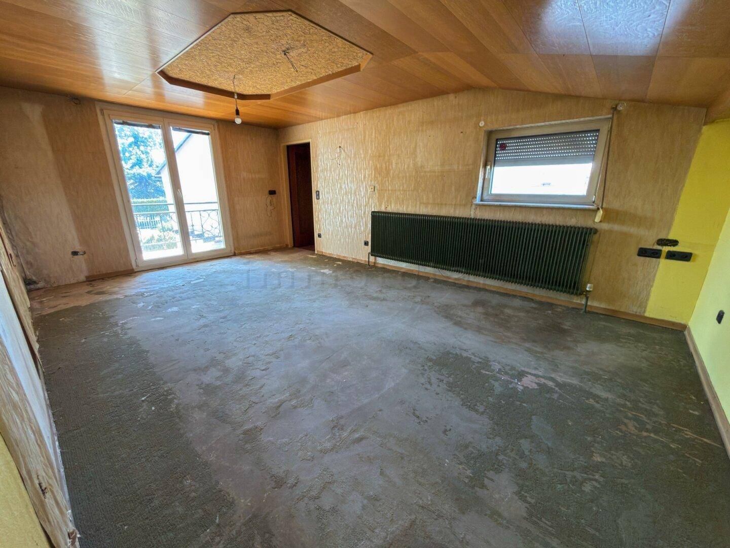 Raum mit unfertigem Boden und Zugang zu einem französischen Balkon, bereit zur Renovierung.