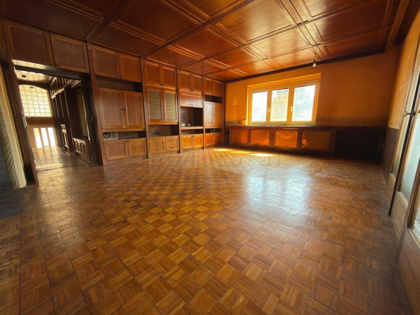 Wohnzimmer mit Holzboden, Holzdecke und integrierten Holzschränken, gut beleuchtet.