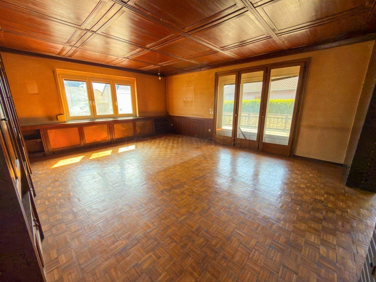 Geräumiges Wohnzimmer mit Fischgrätparkett, Holzdecke und Zugang zum Balkon.