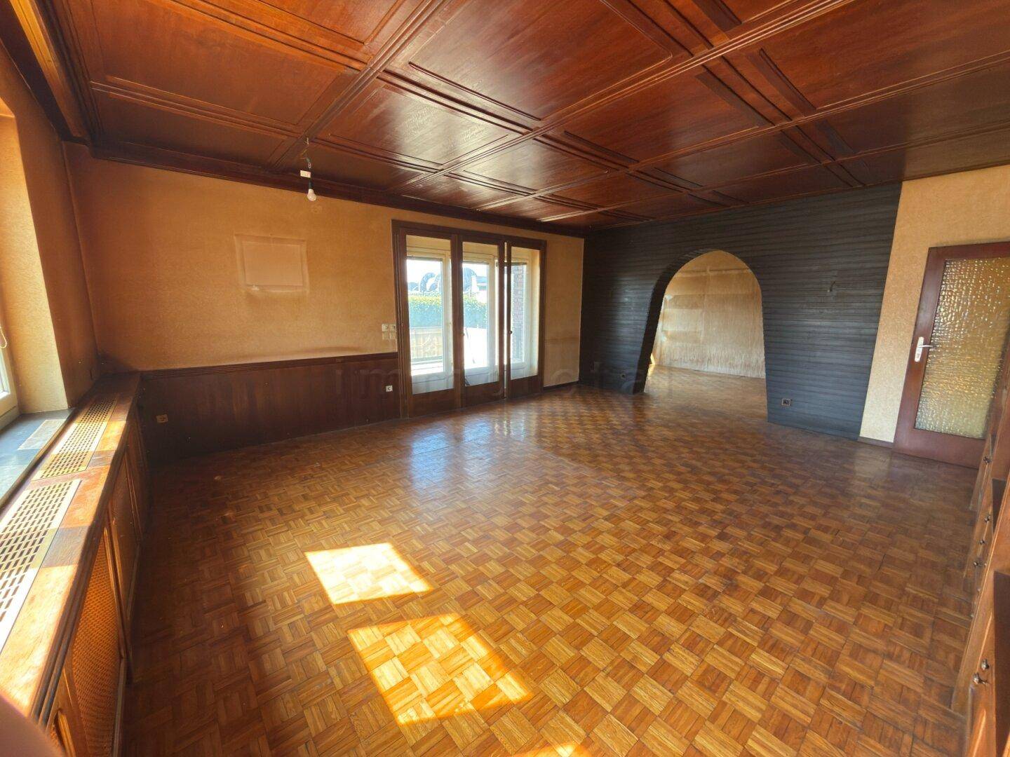 Helles Wohnzimmer mit Holzparkett und Holztäfelung, offen zu einem weiteren Bereich.