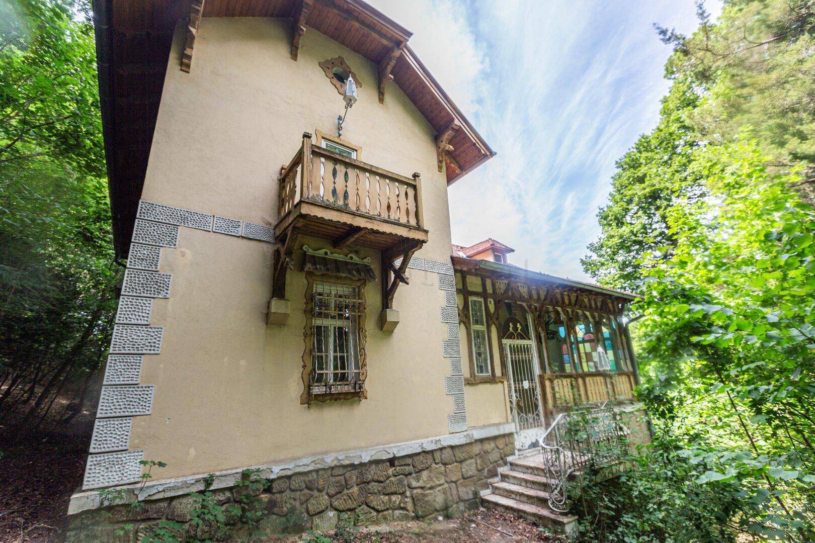 Historisches Gebäude mit dekorativem Holzbalkon und einem einladenden Eingangsbereich im Grünen.
