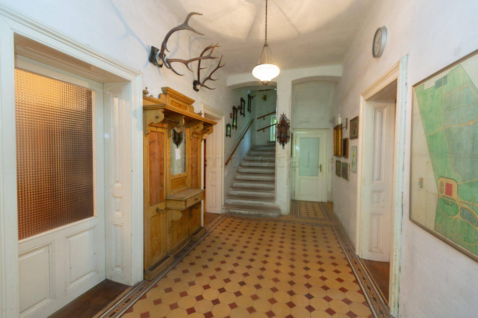 Geräumiger Flur mit gemusterten Fliesen, Holzmöbeln und einer Treppe zum Obergeschoss.