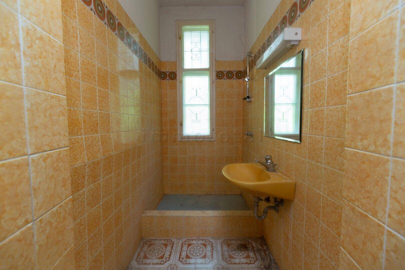 Badezimmer mit gelben Fliesen, einem Waschbecken und einem Fenster, das Tageslicht hereinlässt.