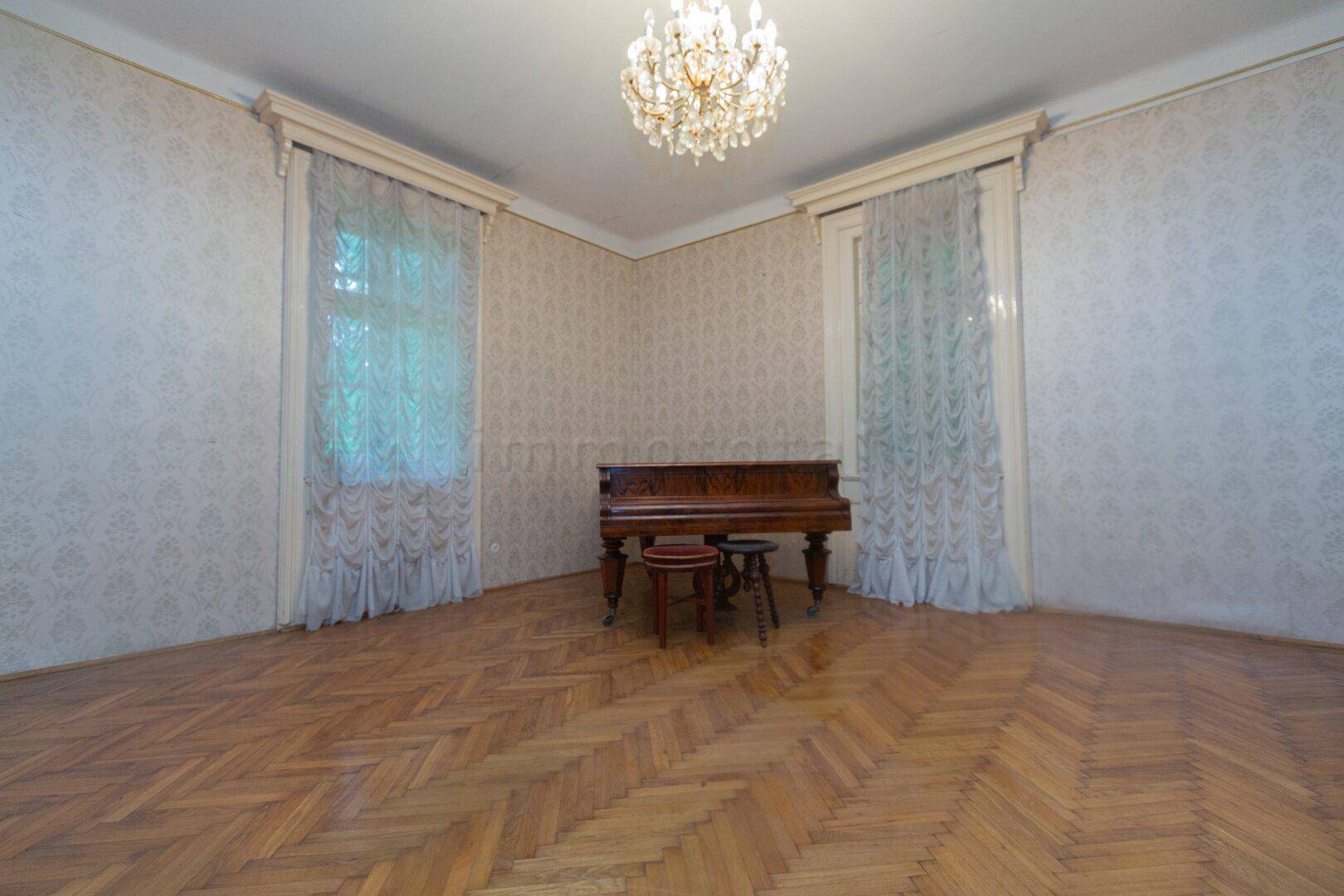 Elegantes Wohnzimmer mit Fischgrätparkett, Kronleuchter und einem antiken Klavier.