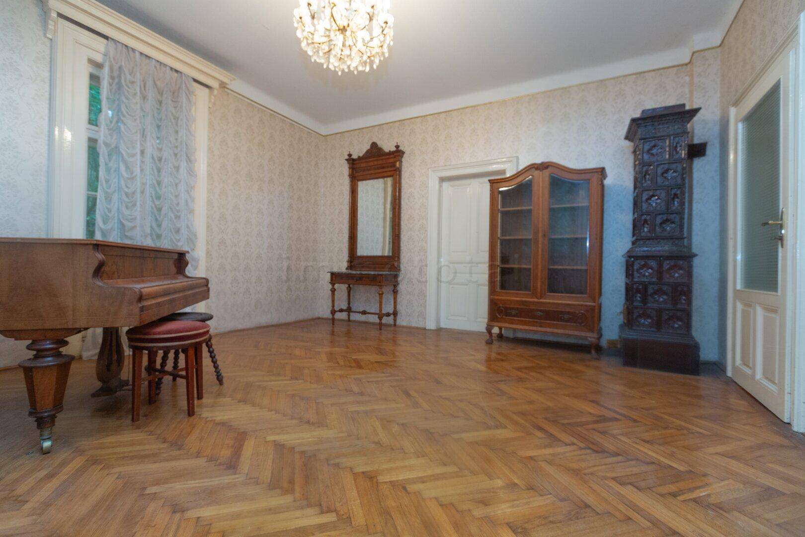 Klassisches Wohnzimmer mit Fischgrätparkett, antiken Möbeln und einem traditionellen Kachelofen.