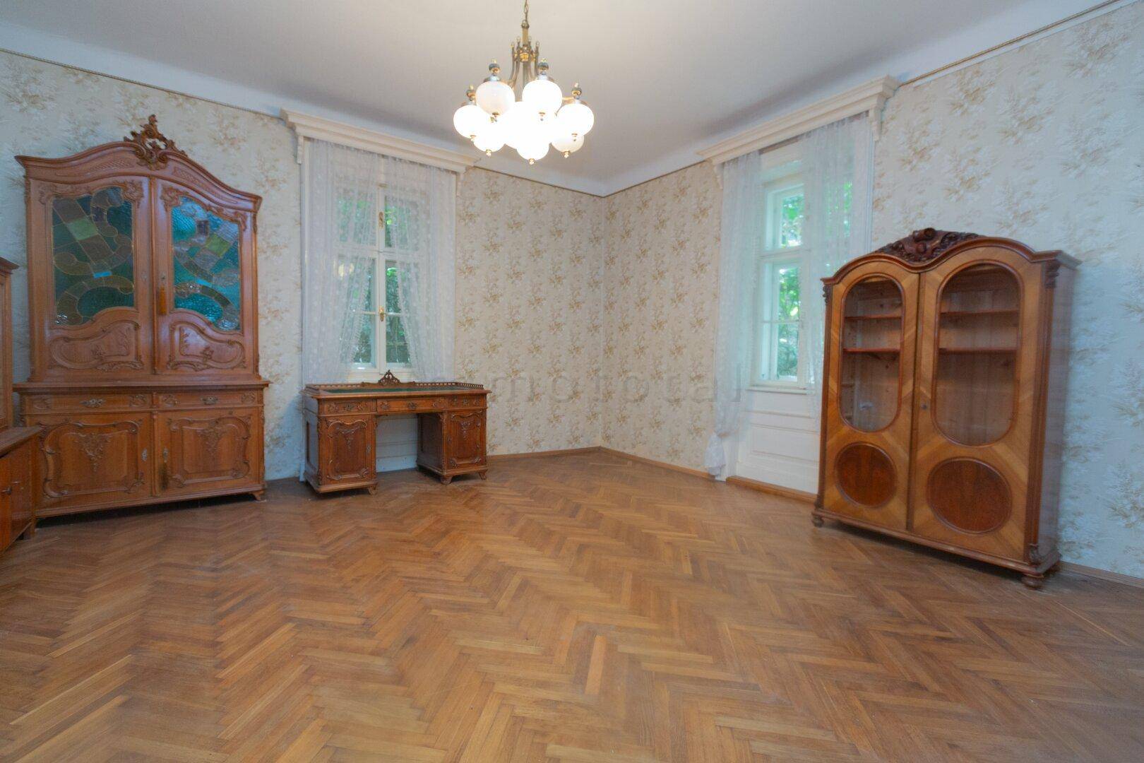 Geräumiges Wohnzimmer mit Fischgrätparkett, antiken Holzschränken und großen Fenstern.