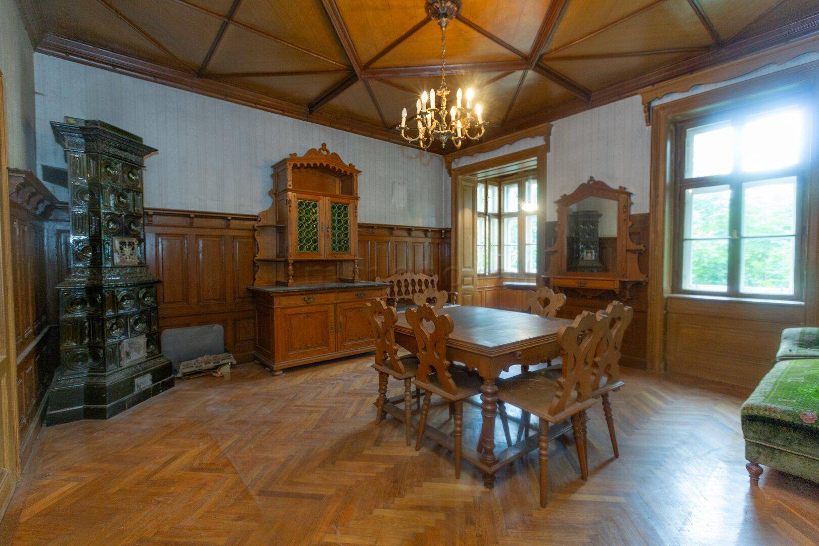 Repräsentativer Essbereich mit Holztäfelung, Kassettendecke, Kachelofen und großem Esstisch.