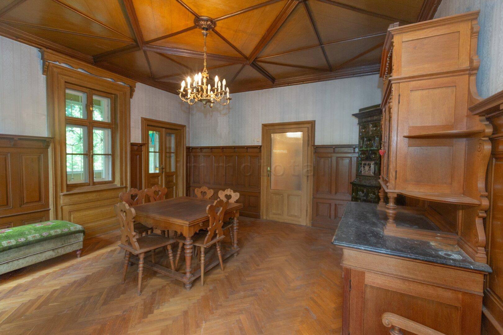 Klassischer Essbereich mit Holztäfelung, Kassettendecke, Kachelofen und traditionellen Holzmöbeln.