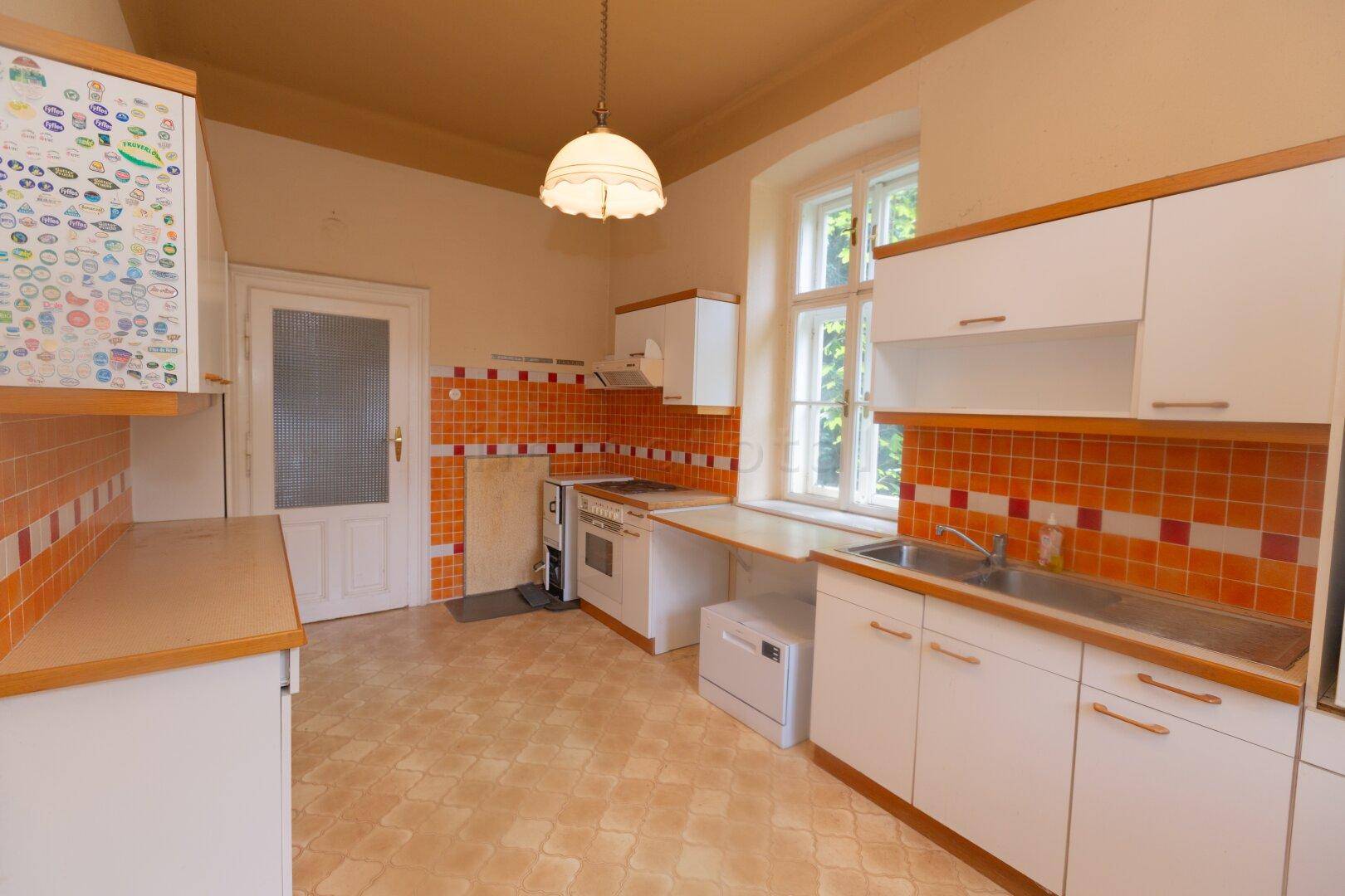 Funktionale Küche mit weißen Schränken, orangefarbenen Fliesen und einem Fenster mit Blick ins Grüne.