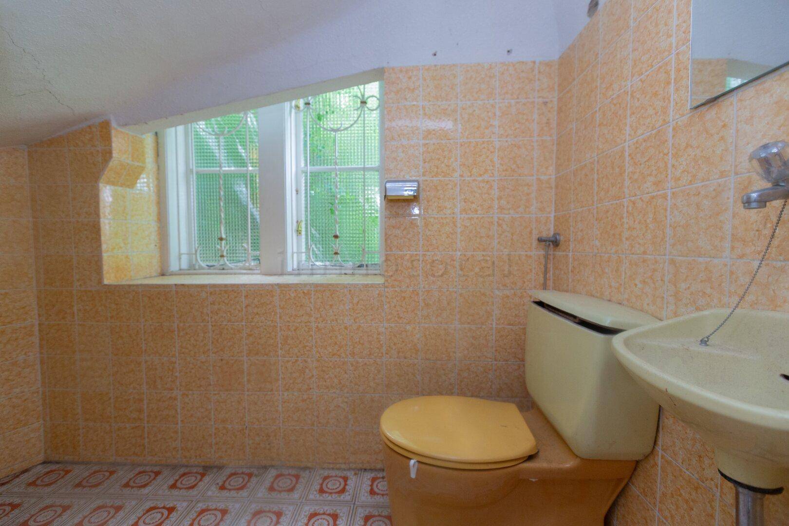 Kleines WC mit gelben Fliesen, passender Toilette und einem Fenster für natürliche Belüftung.