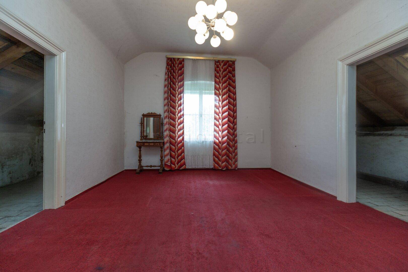 Geräumiges Dachzimmer mit rotem Teppichboden, Dachschrägen und einem Fenster.