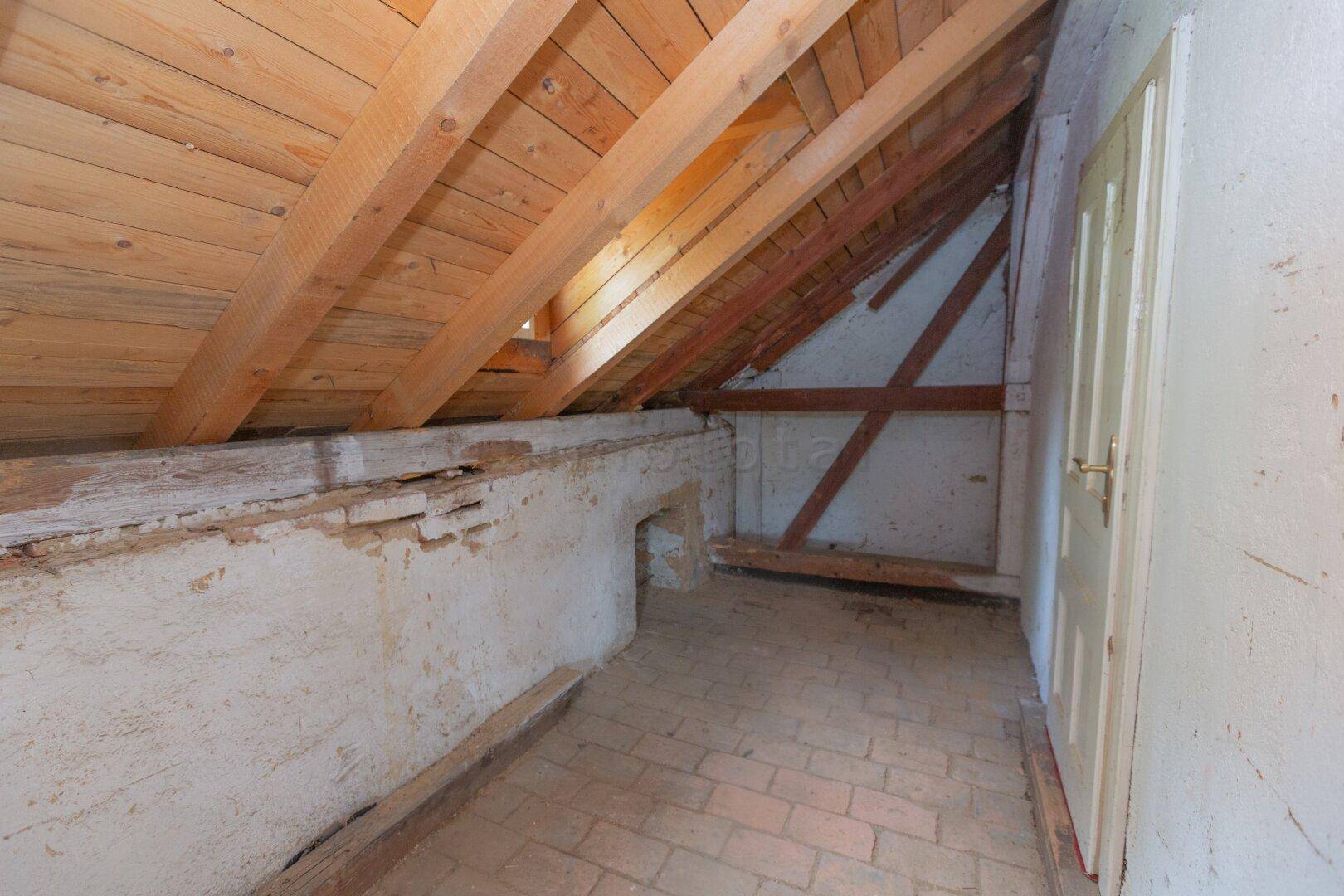 Unausgebauter Dachbodenbereich mit sichtbaren Holzbalken und Ziegelboden.