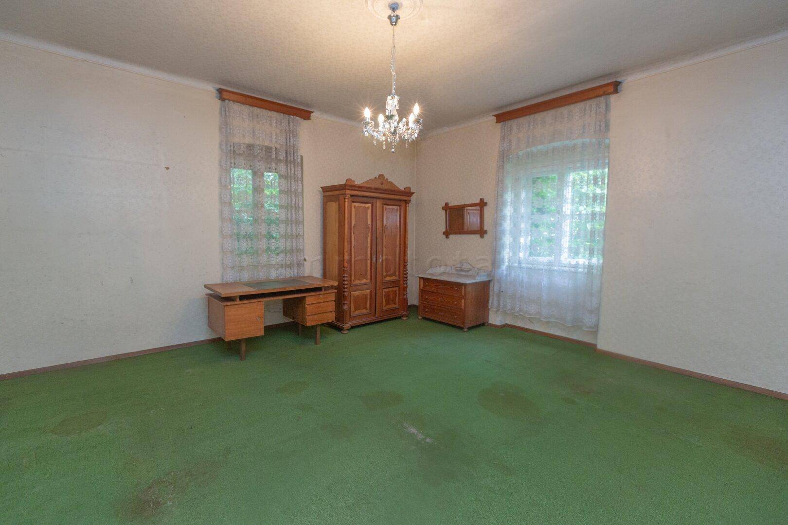 Geräumiges Schlafzimmer mit grünem Teppichboden, antiken Holzmöbeln und Kronleuchter.