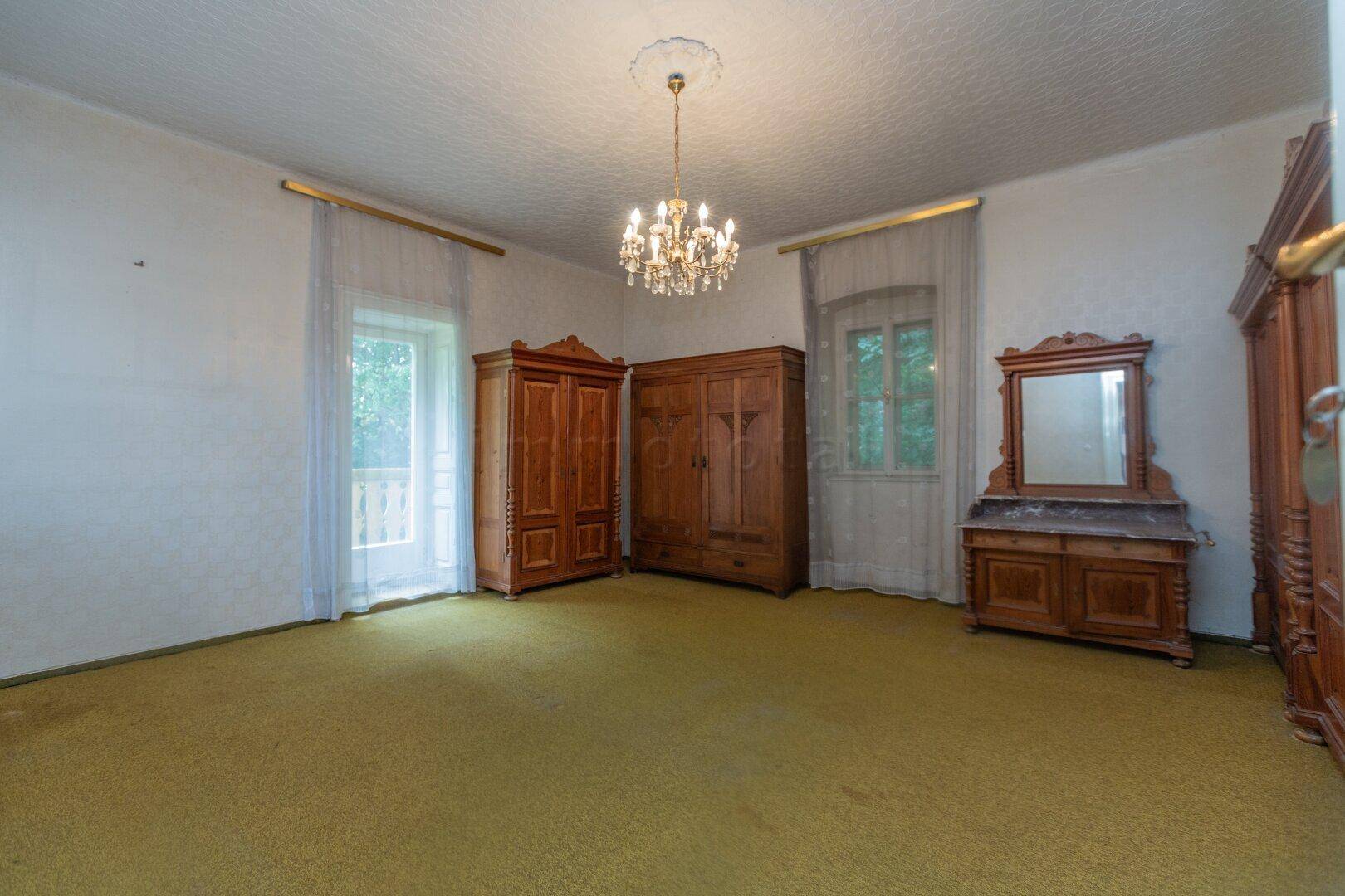 Helles Schlafzimmer mit gelbem Teppichboden, antiken Holzschränken und Zugang zum Balkon.