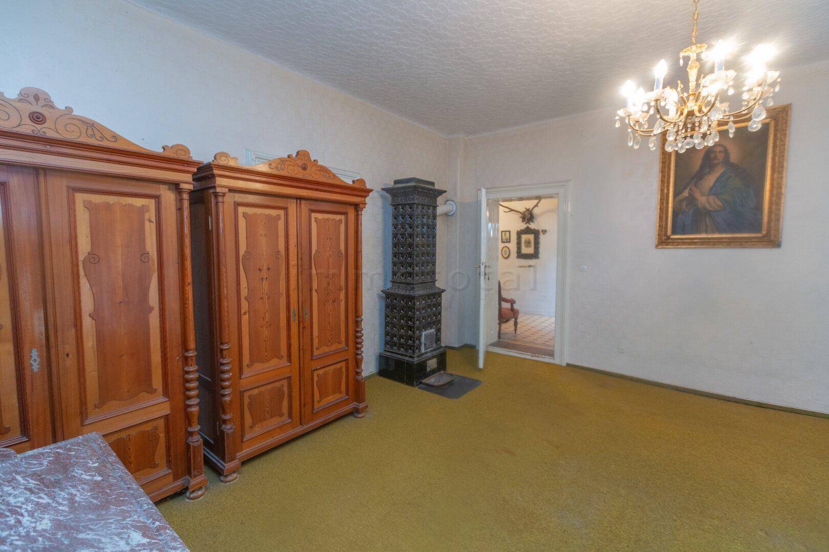 Schlafzimmer mit traditionellem Kachelofen, antiken Holzmöbeln und Kronleuchter.