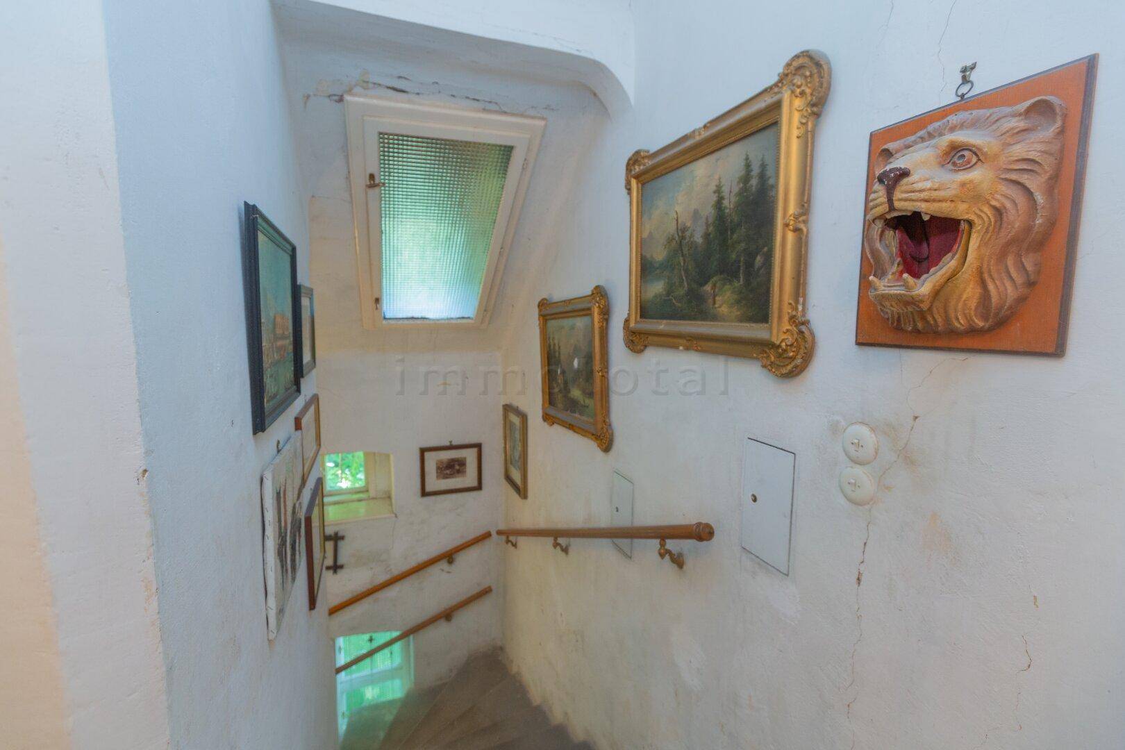 Treppenhaus mit Holzgeländer, Kunstwerken an den Wänden und Dachfenster.