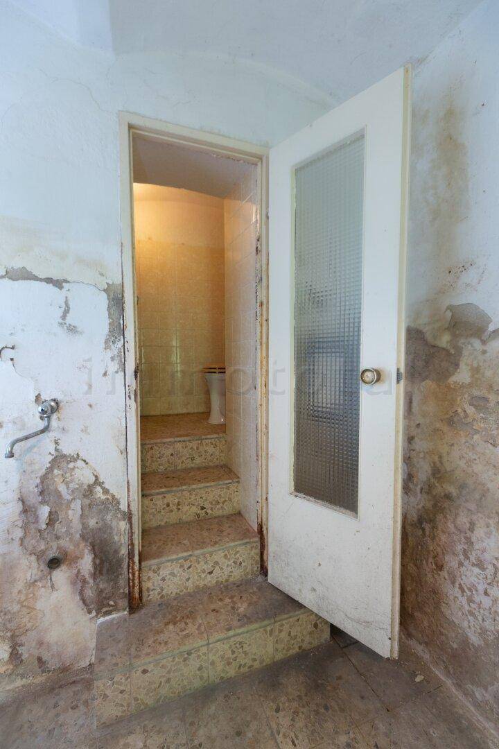 Kleiner Toilettenraum mit Fliesenboden und beschädigten Wänden.
