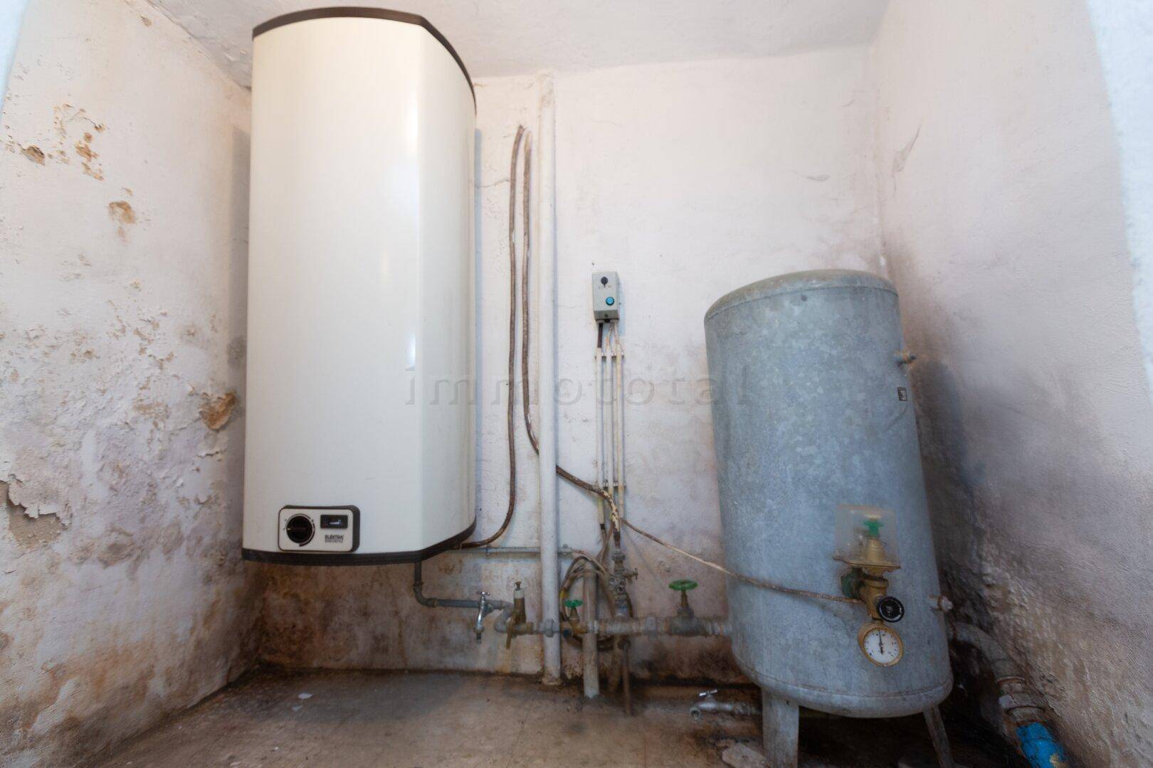 Heizungsraum mit zwei Warmwasserspeichern und sichtbaren Rohrleitungen.