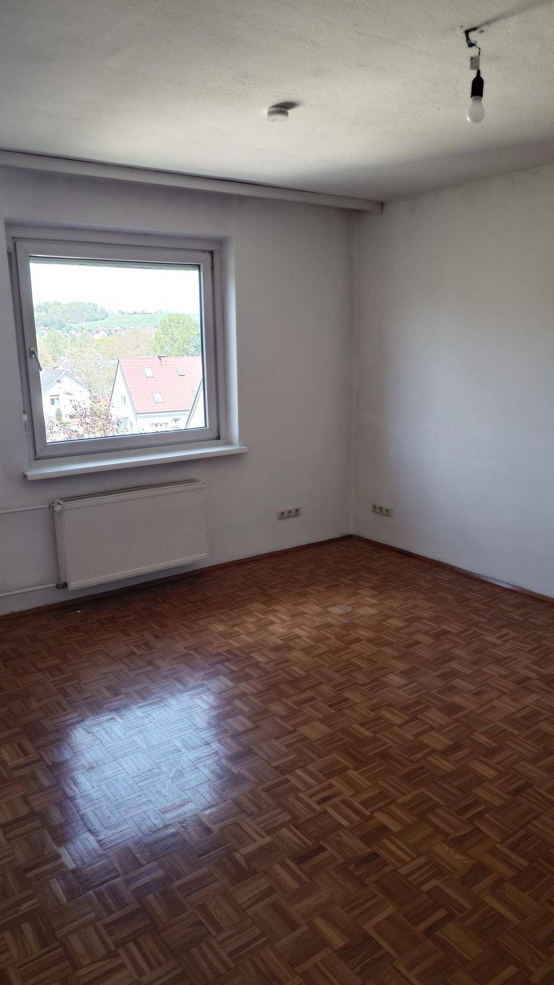 Geräumiger Raum mit Parkettboden und Fenster, ideal für Schlaf- oder Wohnbereich.