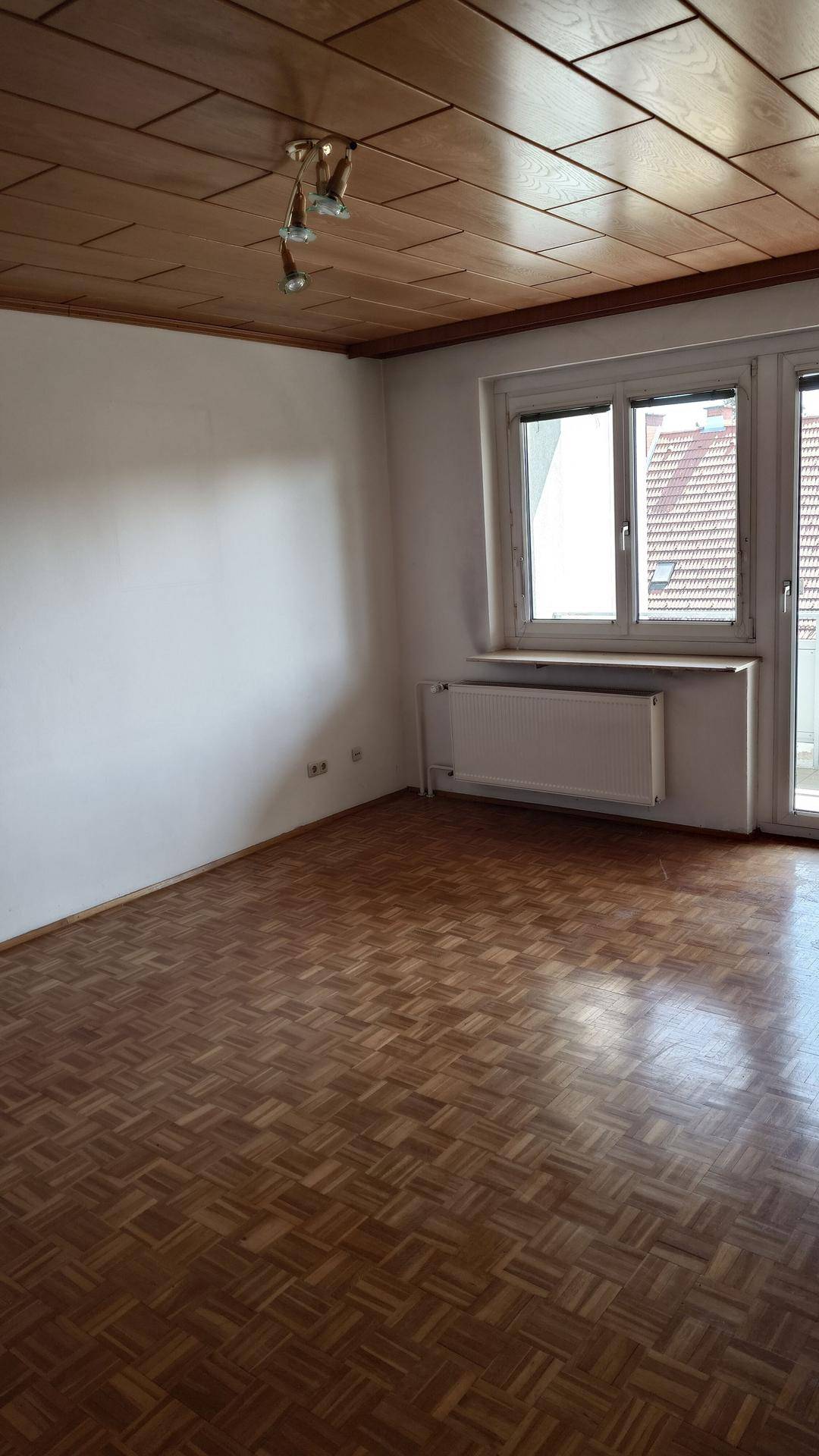 Leerer Raum mit Parkettboden, Holzdecke und Fenster mit Blick auf die Umgebung.