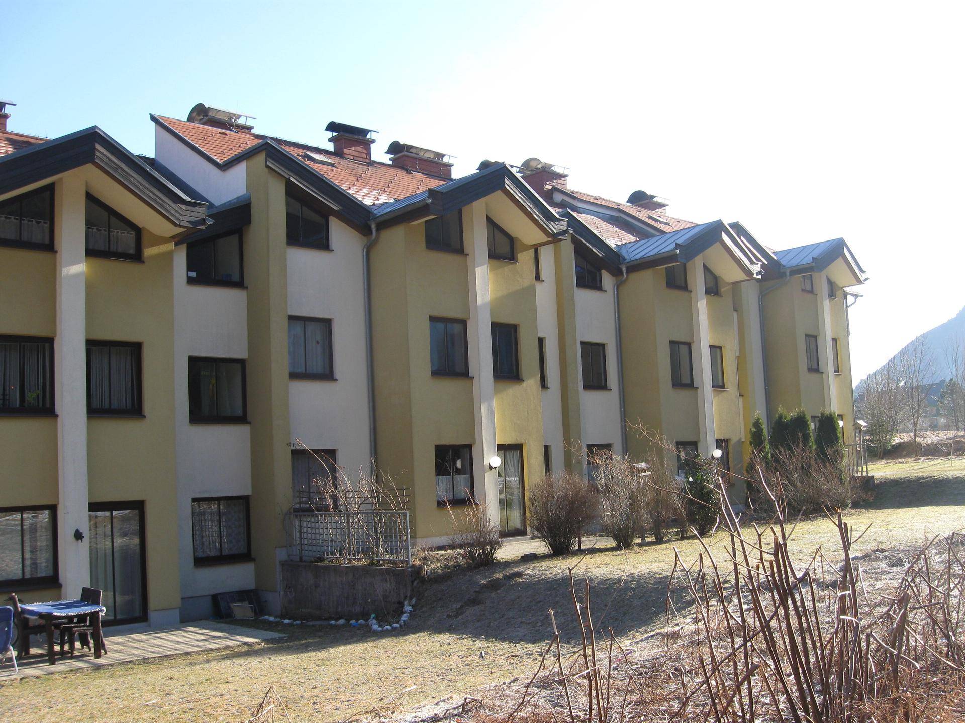 Reihe von Häusern mit gelber Fassade und roten Dächern in einer ländlichen Umgebung.