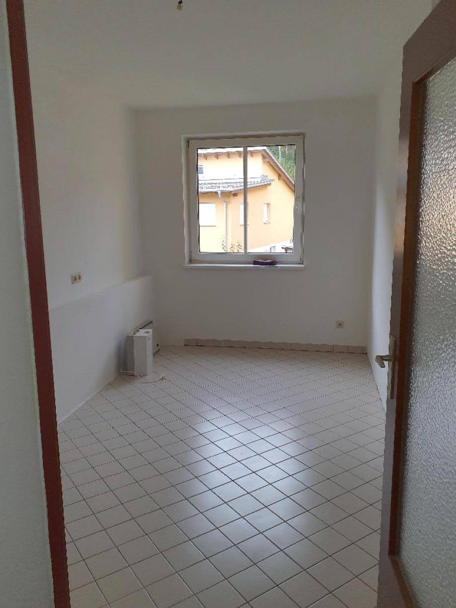 Leeres Zimmer mit hellen Fliesen und einem Fenster, das den Blick auf ein Nachbargebäude bietet.