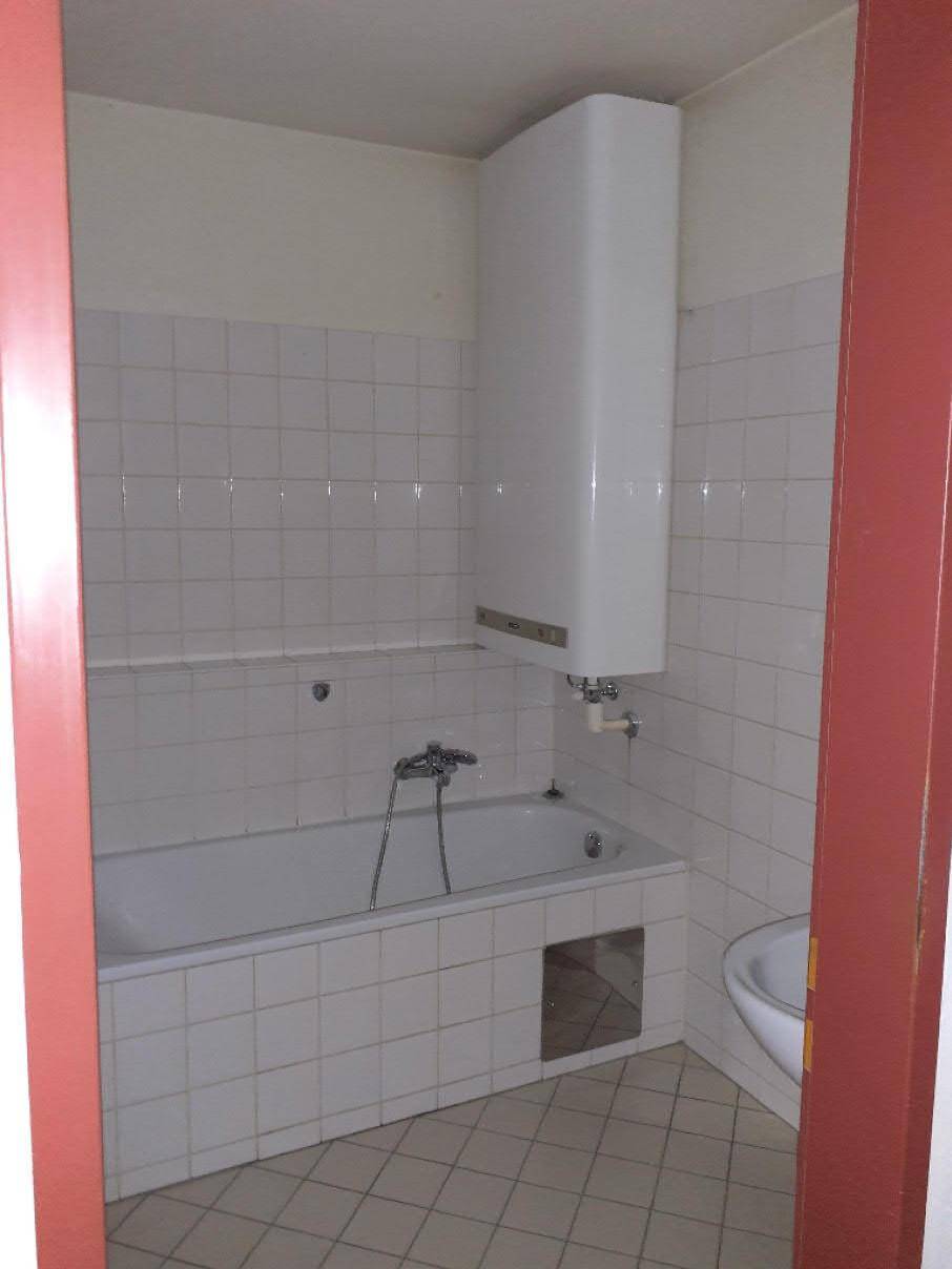 Badezimmer mit Badewanne, weiß gefliesten Wänden und einem Warmwasserboiler, in Standardausstattung.