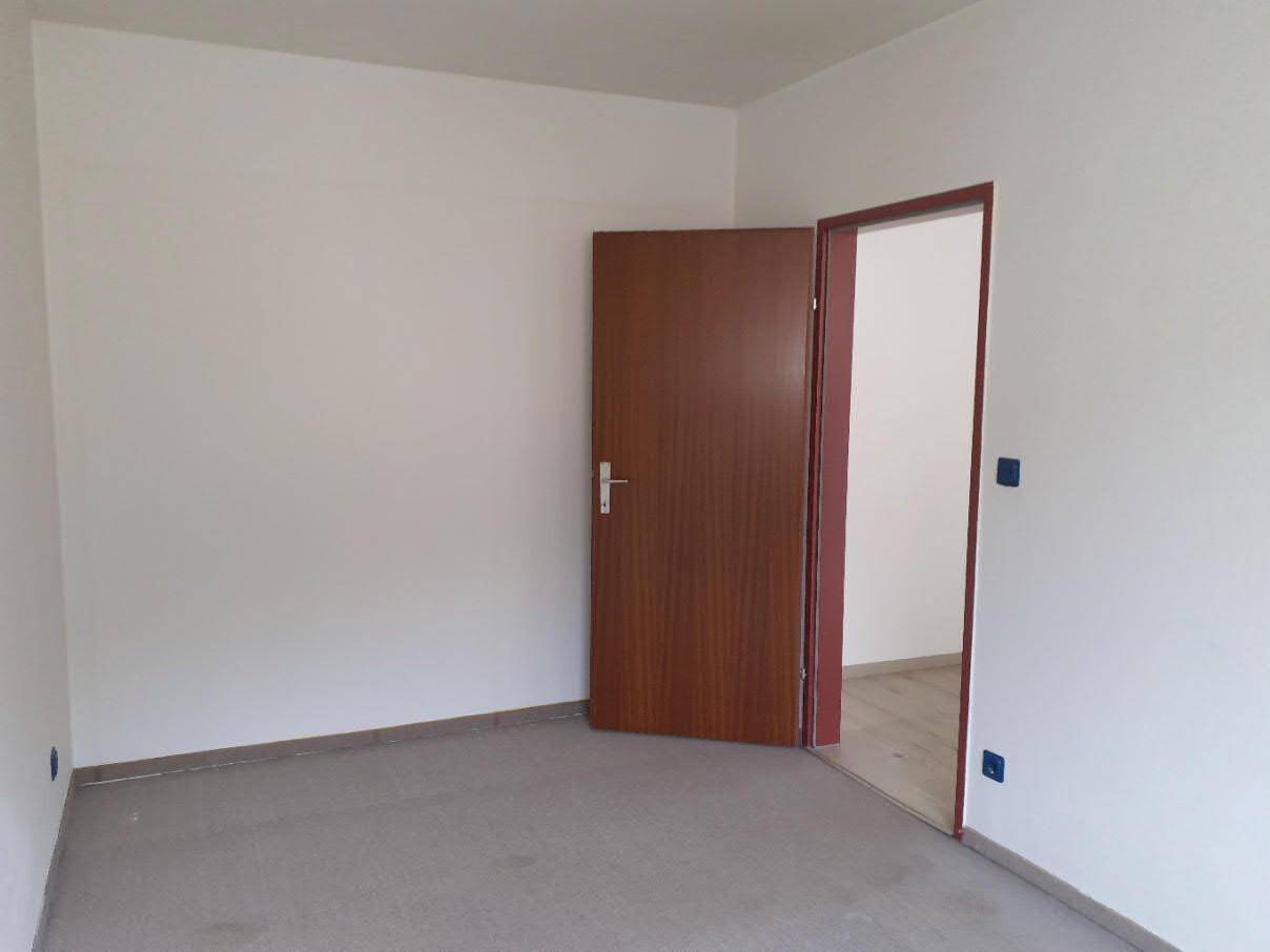 Leeres Zimmer mit hellem Boden und einer offenen Holztür, die den Raum betritt, sehr gepflegt.