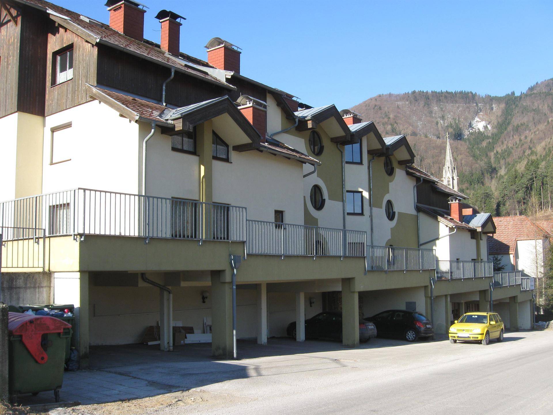 Reihenhäuser mit integrierten Carports und Balkonen, gelegen an einer Straße mit Bergblick.