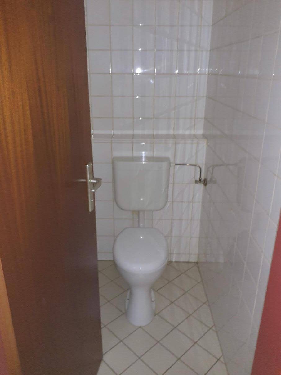 Kleines WC mit weiß gefliesten Wänden und Boden, ausgestattet mit einer Toilette, sehr sauber.