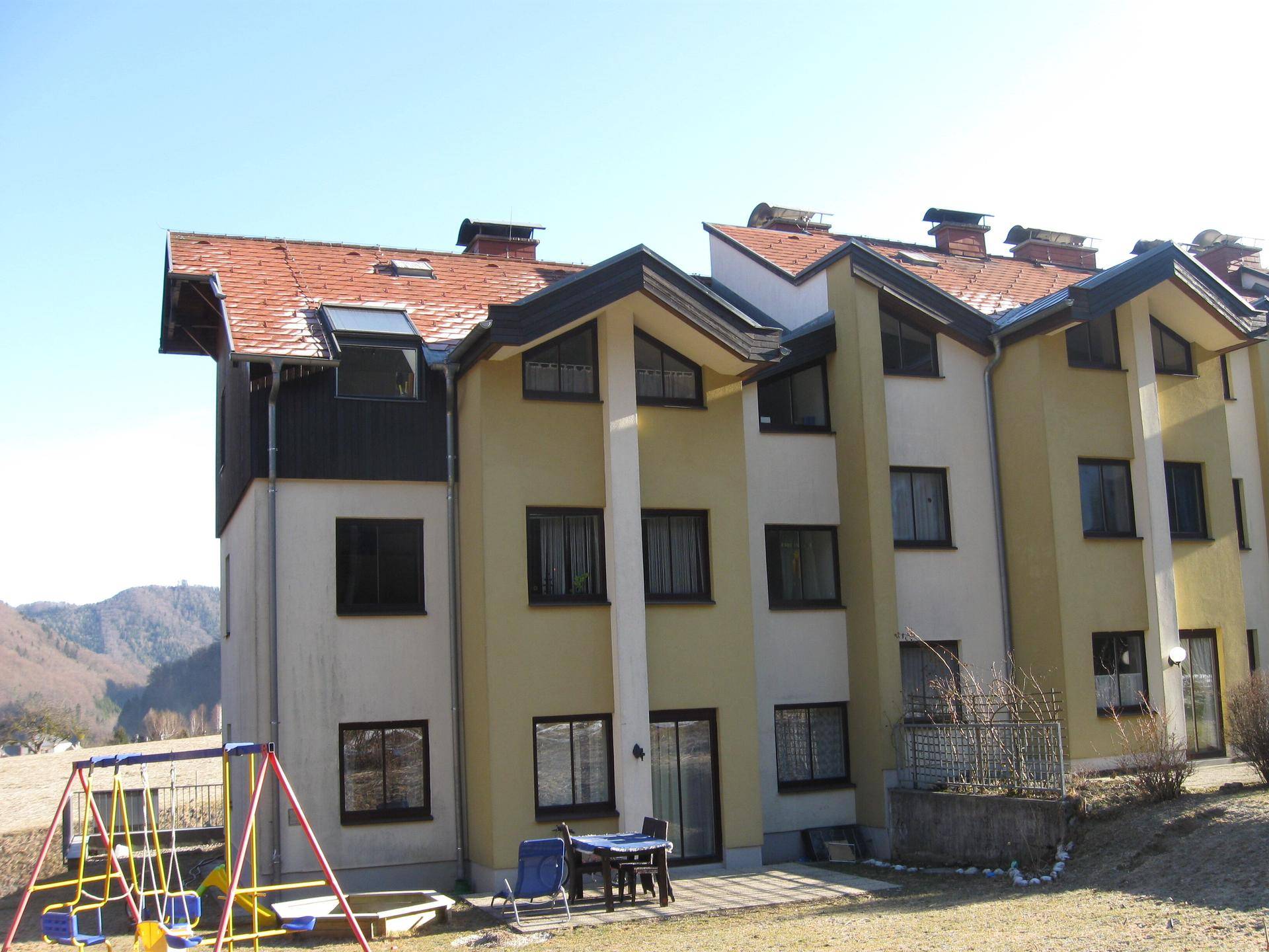 Reihenhäuser mit kleiner Terrasse und Kinderspielplatz im Vordergrund, umgeben von Bergen.