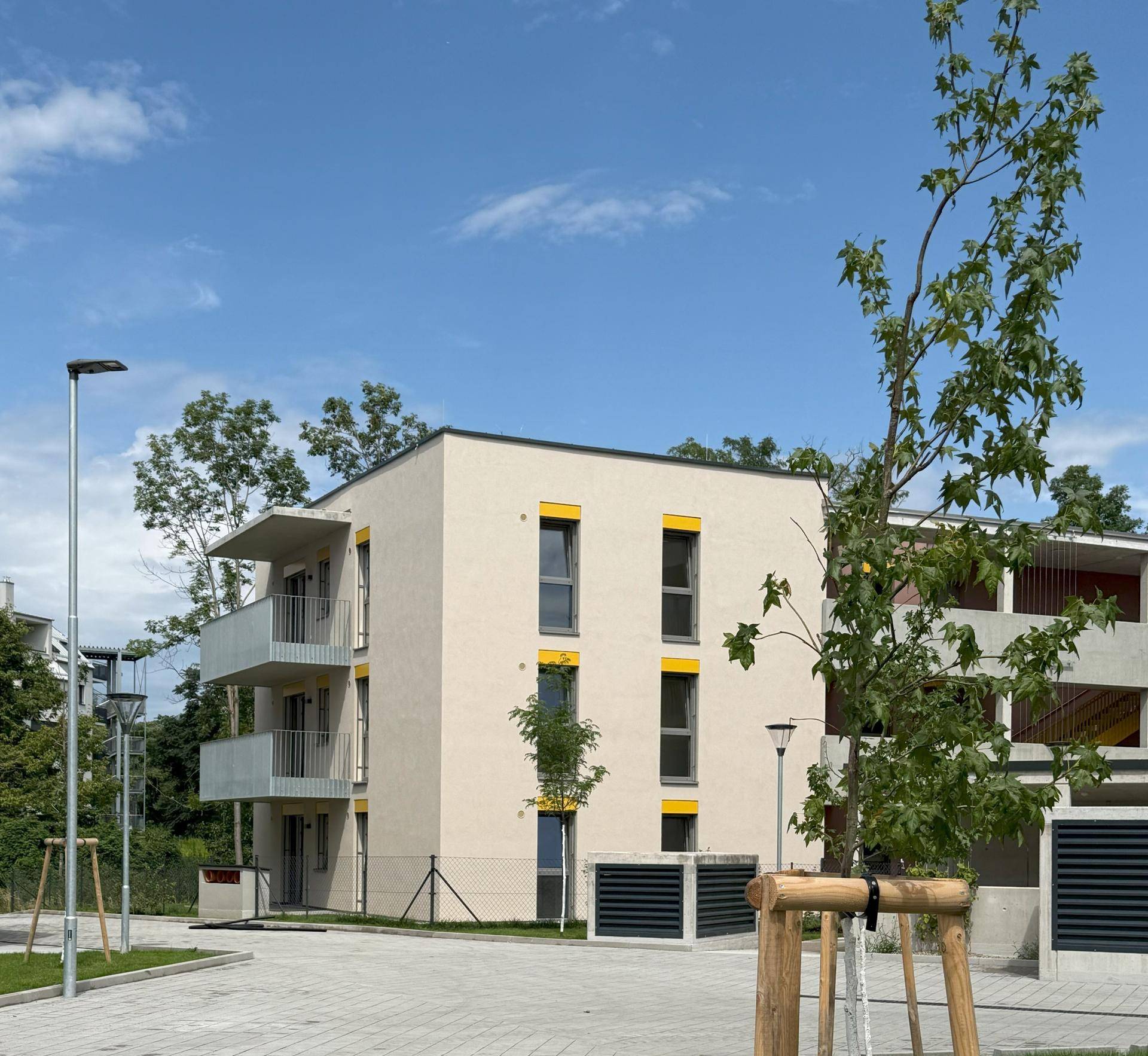 Kleineres Apartmentgebäude mit beigefarbener Fassade, gelben Fensterrahmen und Balkonen unter blauem Himmel.