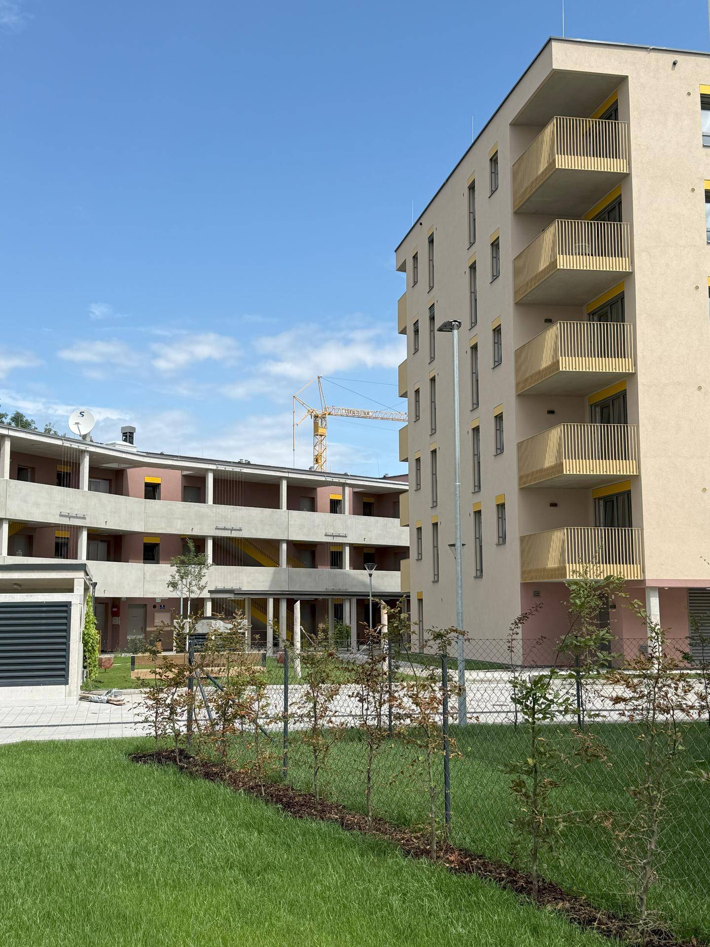 Sonnenbeschienener Apartmentkomplex mit modernen Fassaden, gelben Balkonen und einem Kran im Hintergrund.