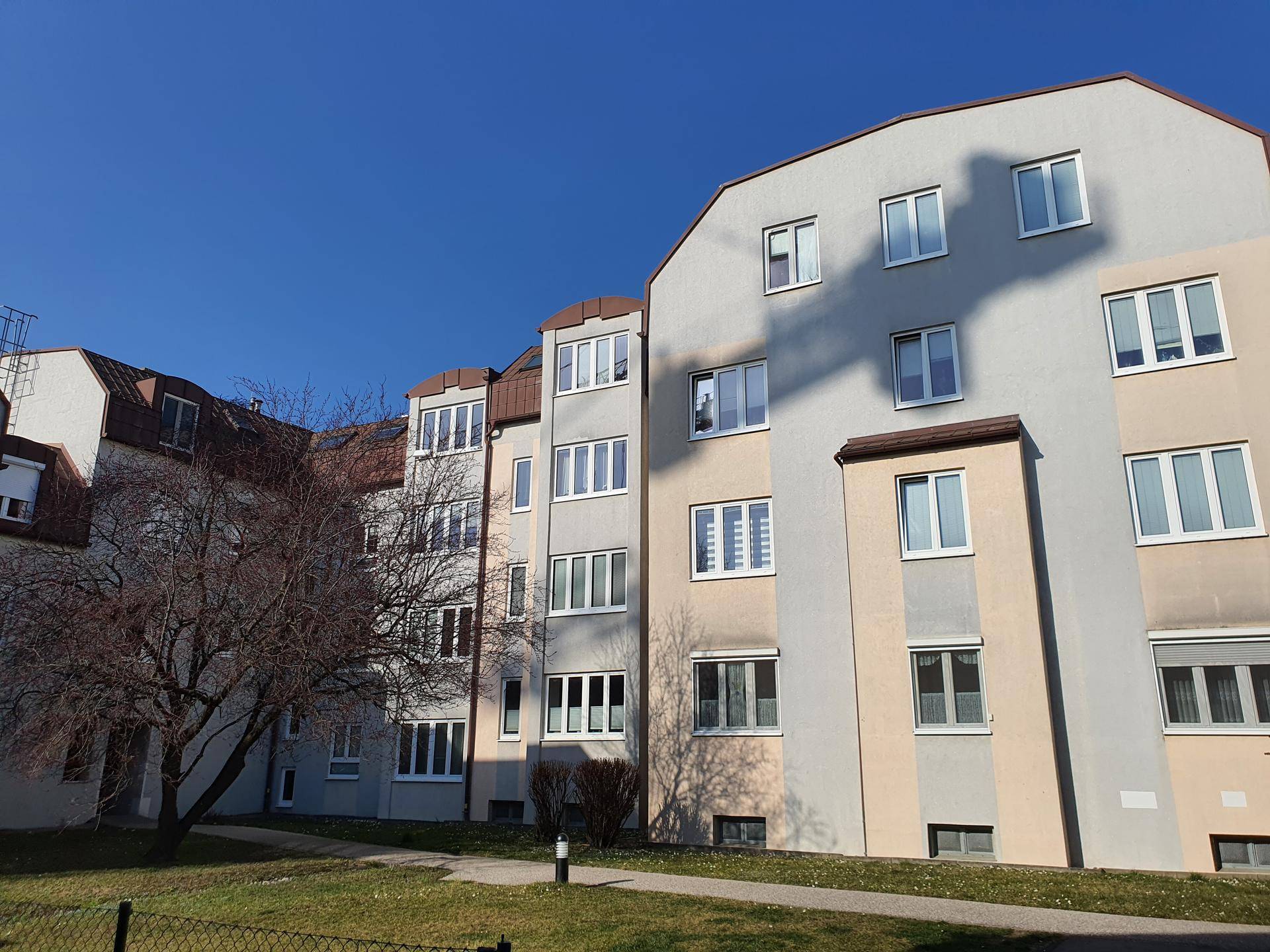 Seitenansicht der Wohngebäude mit hellen Fassaden und zahlreichen Fenstern, umgeben von Rasenflächen.